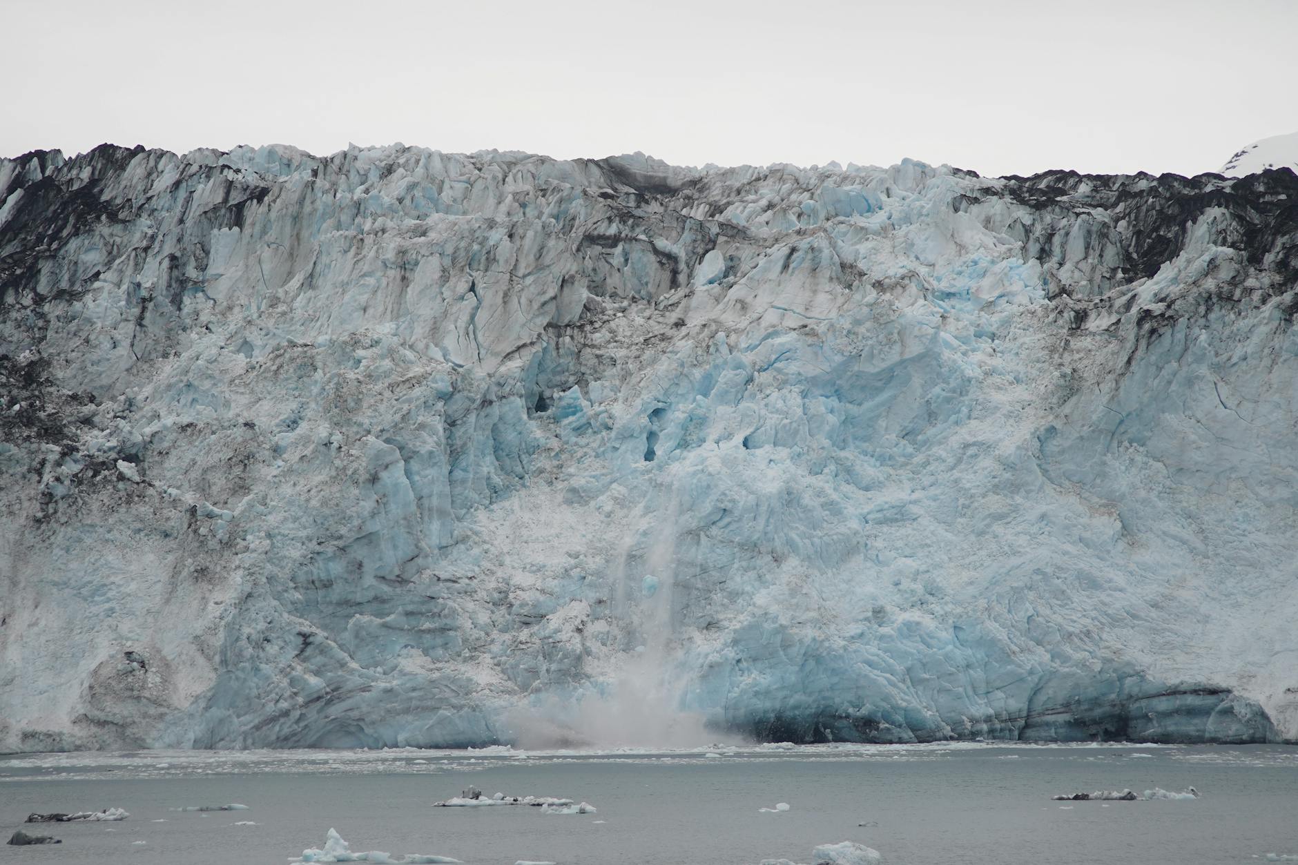 A lone scientist braves a blizzard on a vast, icy glacier, his figure dwarfed by the immense landscape.